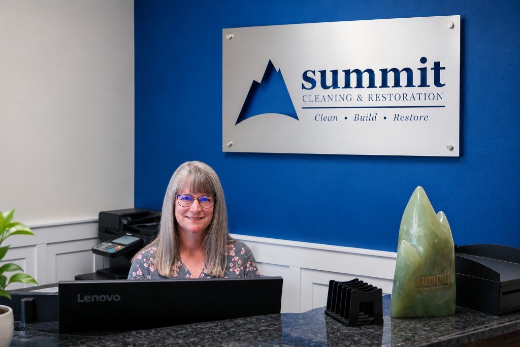 Sandra at the Summit Cleaning & Restoration front desk, beneath the lobby sign, ready to take a call